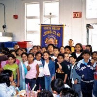 11/22/05 - Mission Educational Center, San Francisco - Students crowd in for a group shot with our Club banner. Lion Bob Lawhon patiently waits just in front of the banner for them to get set.