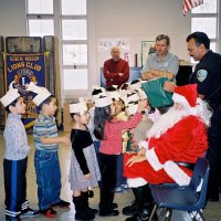 12/15/06 - Christmas at Mission Educational Center, Police Officer “Nacho” Martinez as Santa - Santa, assisted by his Police Officer escorts, greets and presents each student with gifts. Lions Bill Graziano (red sweater) and Bob Fenech, on his left, look on.