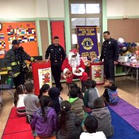 12/21/17 - Christmas with Santa, Mission Educational Center - San Francisco Firemen escort, from the SFFD Toys for Tots Program, look on as Santa talks with the school children.