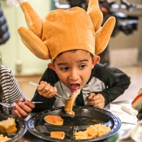 11/16/17 - Serving Thanksgiving Luncheon, Mission Educational Center - An immigrant student wearing a turkey hat feasts on turkey lunch during his first Thanksgiving at Mission Education Center. (Mira Laing/Special to S.F. Examiner)