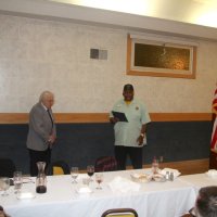 3-20-24 - Italian American Social Club, San Francisco - District Governor’s Visitation, Joe Farrah’s 58 Year Recognition - District Govenor Kevin Guess, on the right, quoting Lion Joe Farrah’s Lions resume and accomplishments.