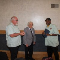 3-20-24 - Italian American Social Club, San Francisco - District Governor’s Visitation, Joe Farrah’s 58 Year Recognition - 1st VDG Clayton Jolley, left, joins DG Kevin Guess, right, in present Lion Joe Farrah, center, with a special pin received from Lions International.