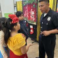 12-18-24 - 43rd Annual Lions Christmas with Santa at the Mission Education Center with Los Bomberos Firefighters - A member of Los Bomberos Firefighters chating with students before the festivities.